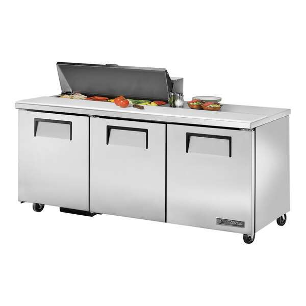 A True TSSU-72-10-HC refrigerated sandwich prep table with three doors and food on top.