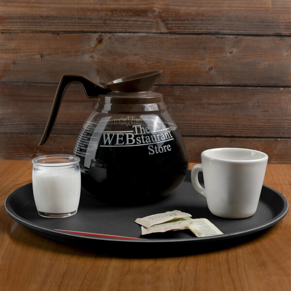 A Cambro black non-skid serving tray with a coffee pot, milk, and a cup on it.