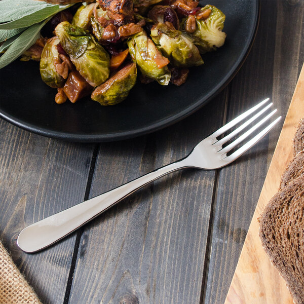 A plate of brussels sprouts and bacon with bread next to a Walco European table fork.