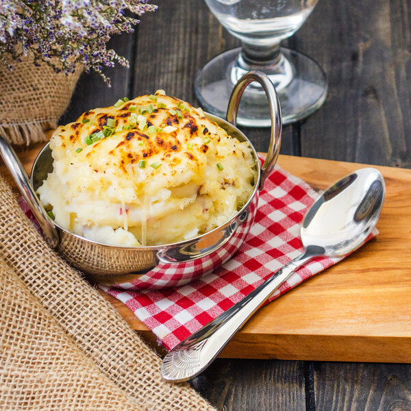 A bowl of mashed potatoes with a Walco Art Deco stainless steel teaspoon on a wooden board.