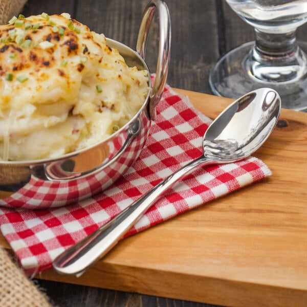 A bowl of mashed potatoes with a Walco stainless steel teaspoon on a red and white checkered napkin.