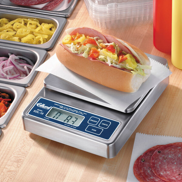An Edlund digital portion scale weighing a hot dog with vegetables on a tray.