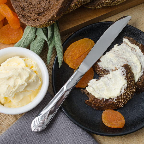 A plate with a Walco Art Deco stainless steel solid handle butter knife, a piece of bread with butter, and dried apricots.