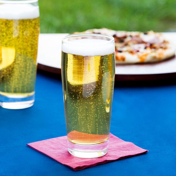Two Arcoroc Willi Becher pub glasses of beer on a table with a pizza.