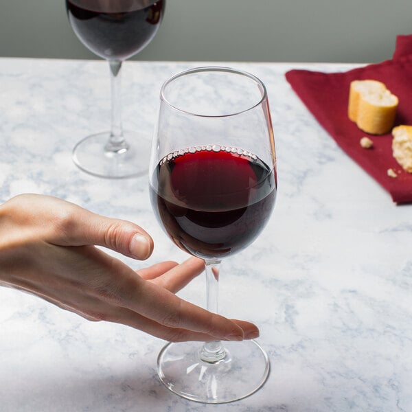 A hand holding a Reserve by Libbey wine glass full of wine on a table.