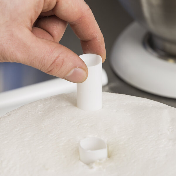 A hand using a Wilton plastic cake dowel rod to support a cake.