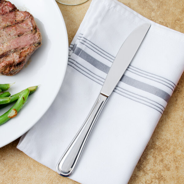 A Walco stainless steel dinner knife on a napkin next to a plate of steak and green beans.