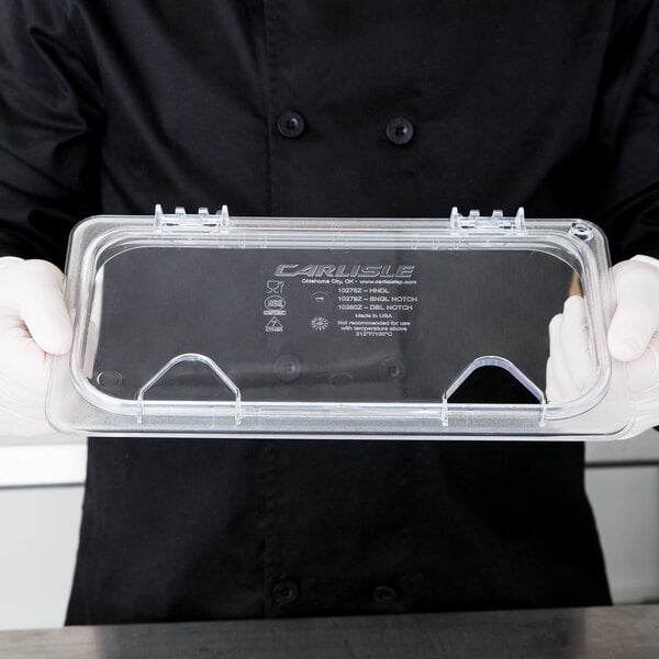 A person in a chef's uniform holding a Carlisle clear plastic container with a hinged lid.