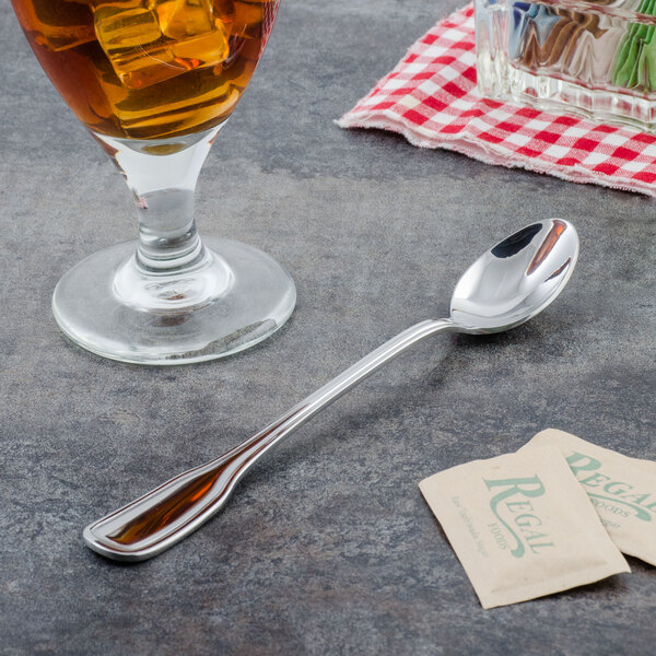A Walco Saville iced tea spoon next to a glass of liquid.