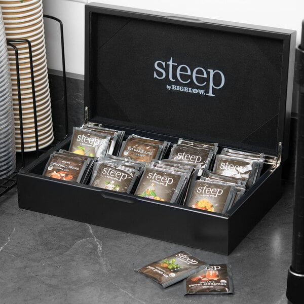A Steep by Bigelow black tea chest on a table with brown packages of tea.