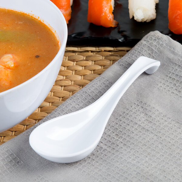 A bowl of soup with a white Thunder Group melamine Asian soup spoon.