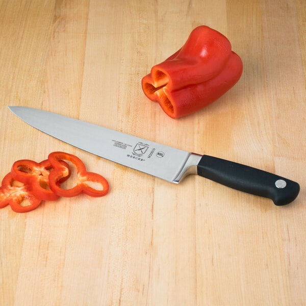 A Mercer Culinary Genesis chef knife on a cutting board next to sliced red bell peppers.