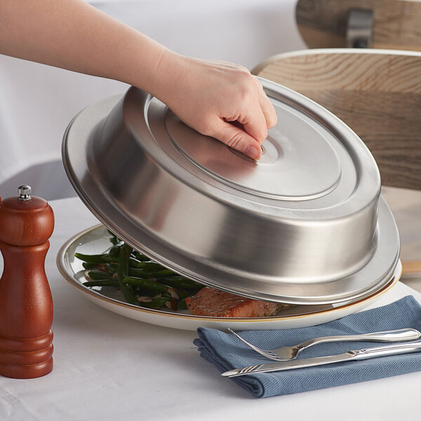 A person holding a Vollrath stainless steel dome plate cover over a plate of food.