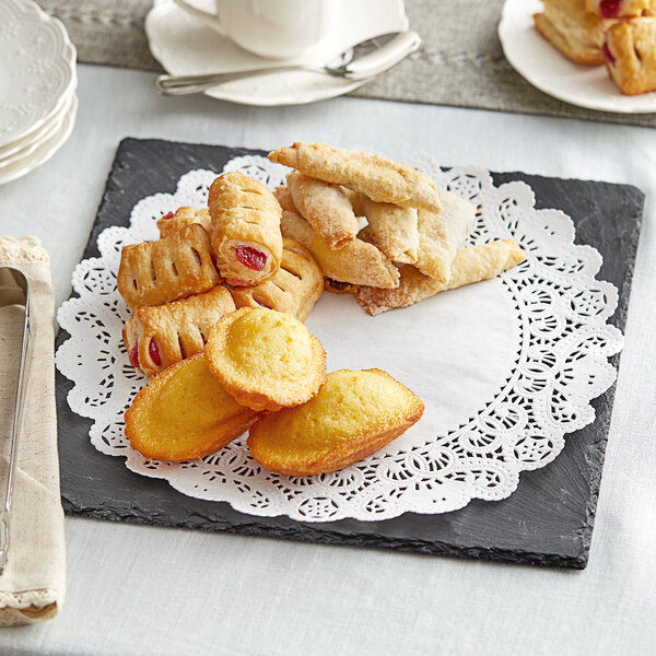 A white plate with a black border and Normandy Lace doilies on a table with pastries and coffee.