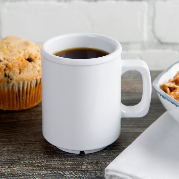 A white Thunder Group melamine mug filled with brown liquid next to a muffin.