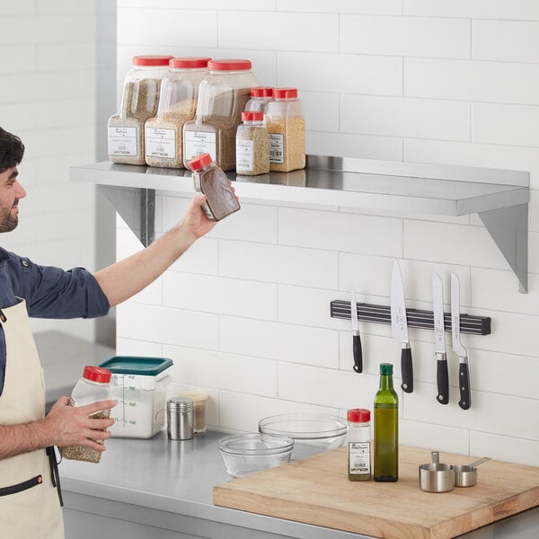 A man holding a plastic container of spices on a Regency stainless steel wall shelf.