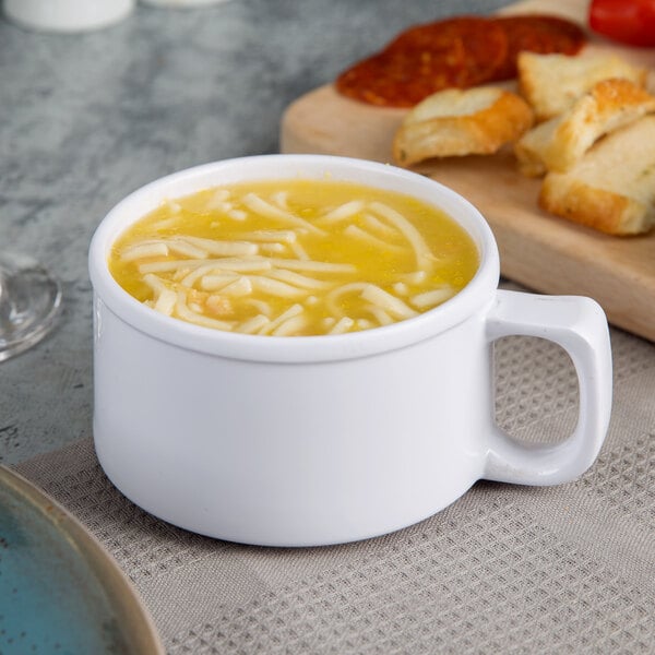 A white Thunder Group melamine soup mug with soup in it next to a plate of bread.