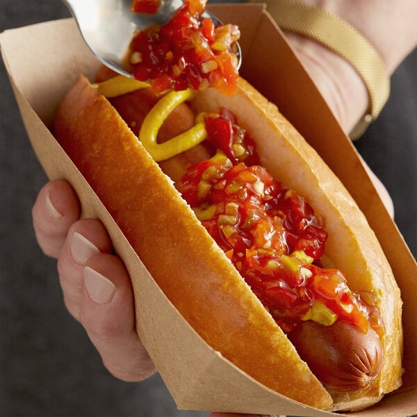A person using a spoon to put Del Sol Pepper Relish on a hot dog.