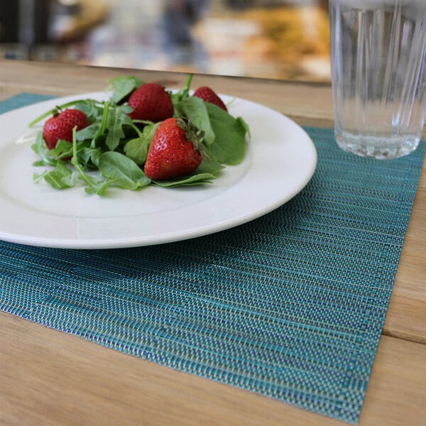 An aqua woven vinyl rectangle placemat with a plate of strawberries and leaves on it.