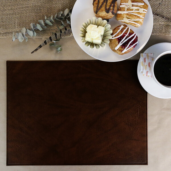 A white plate with pastries and a cup of coffee on a brown faux leather placemat.