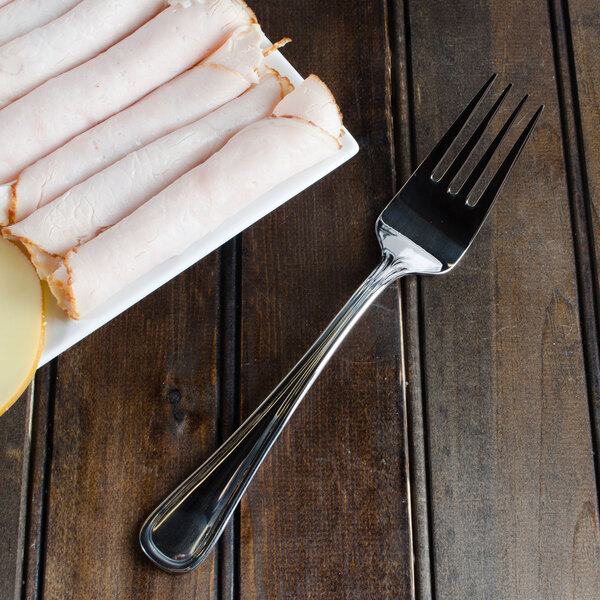 A Walco stainless steel cold meat fork on a plate of sliced meat.