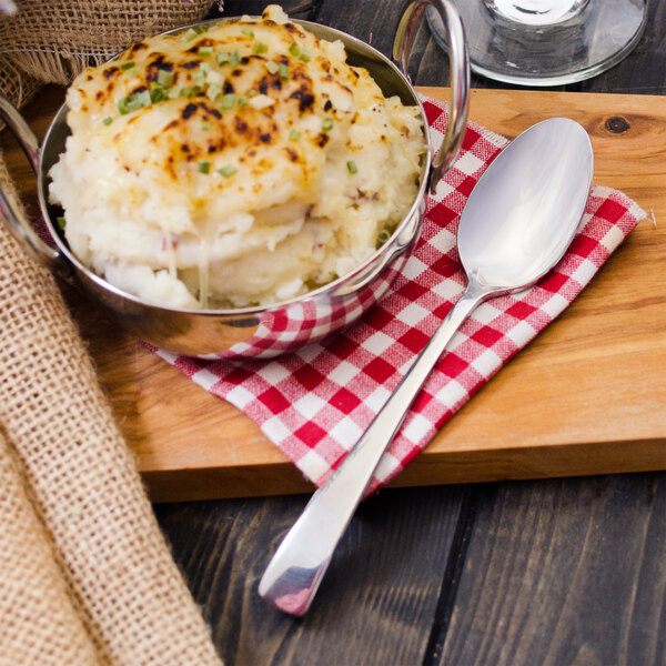 A bowl of mashed potatoes and a Walco Freya stainless steel teaspoon on a wooden board.