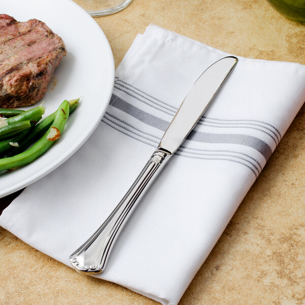 A plate of meat and green beans with a Walco stainless steel table knife on a napkin.