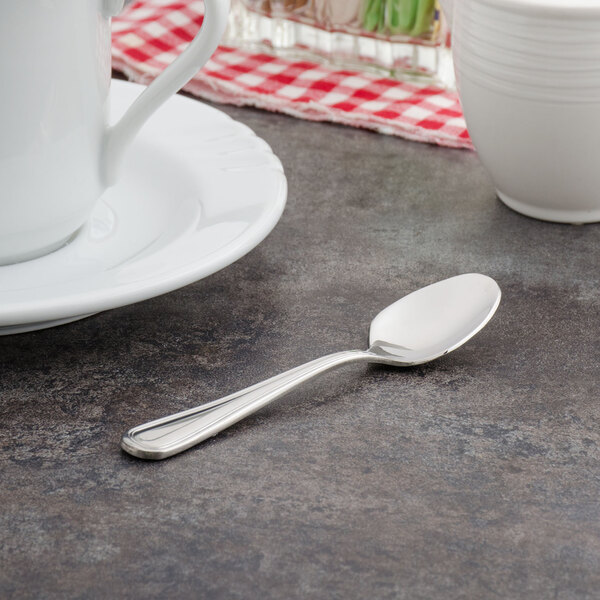 A Walco stainless steel demitasse spoon on a table next to a white cup of coffee.
