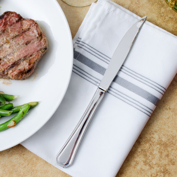 A Walco stainless steel steak knife on a plate of steak and green beans.