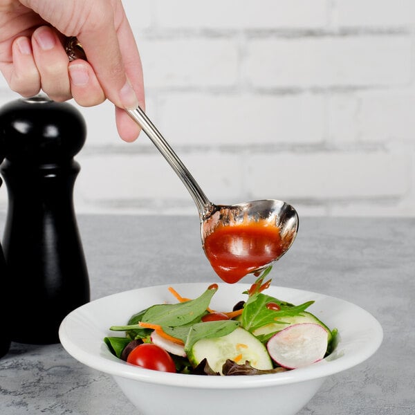 A hand using a Walco stainless steel gravy ladle to pour sauce over a bowl of salad.
