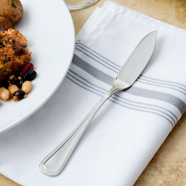A Walco stainless steel fish knife on a napkin next to a plate of food.