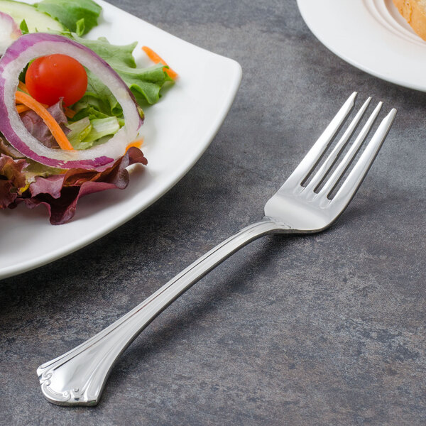 A Walco stainless steel salad fork next to a plate of salad.