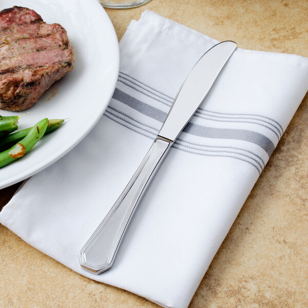 A Walco European table knife on a napkin next to a plate of steak and green beans.