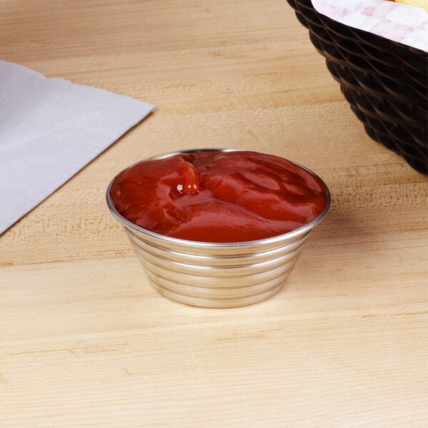 An American Metalcraft stainless steel round ribbed sauce cup filled with ketchup on a table.