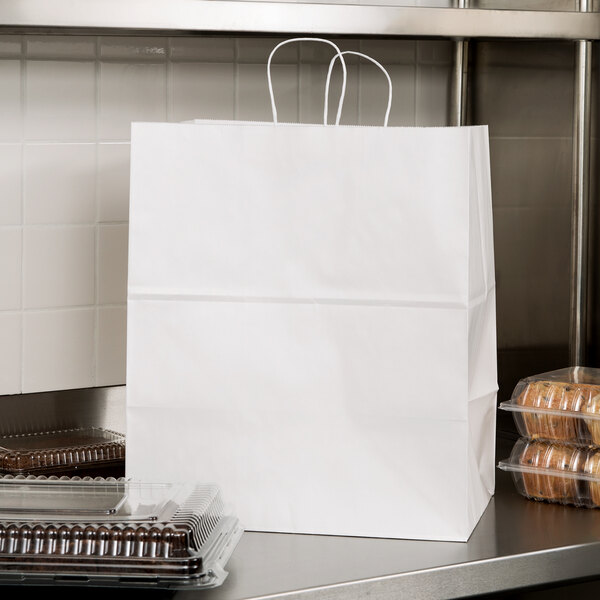 A white Duro paper shopping bag with handles on a table with plastic containers inside.