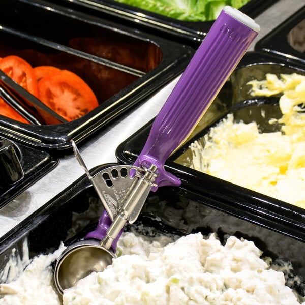A Vollrath Jacob's Pride purple thumb press ice cream scoop on a tray of food.