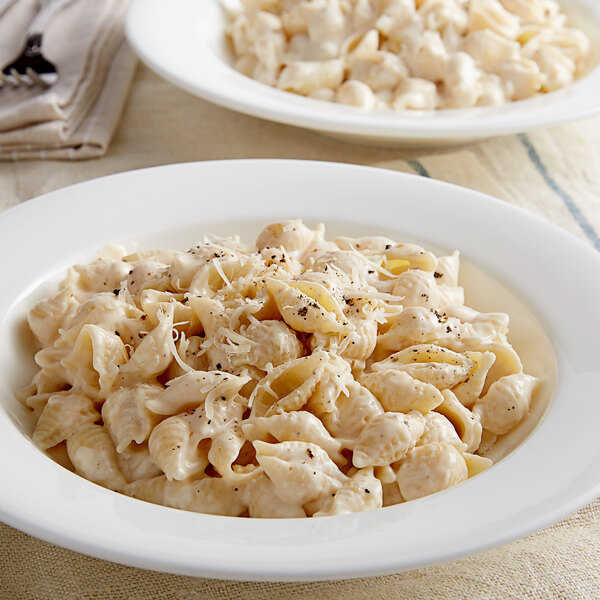 Two white bowls of shell pasta with cheese and herbs.