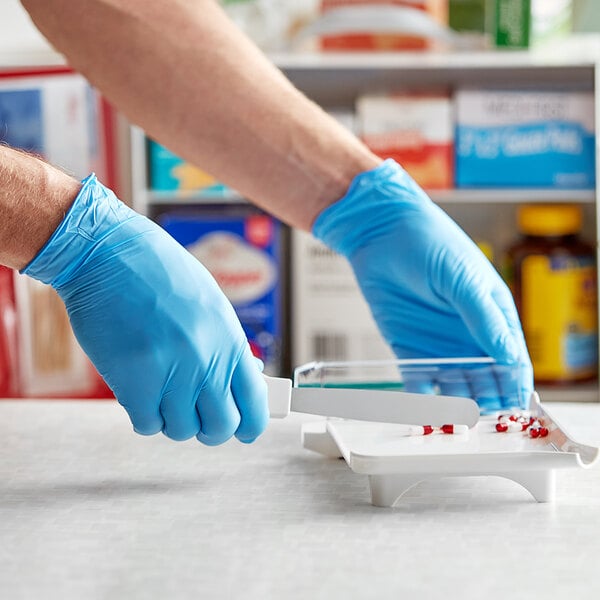 A person wearing Noble Products blue gloves using a knife to cut pills on a white plate.