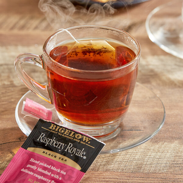 A glass cup of Bigelow Raspberry Royale tea with a tea bag on the table.