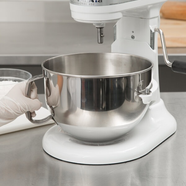 A gloved hand using a silver KitchenAid mixing bowl with a handle to mix white powder.