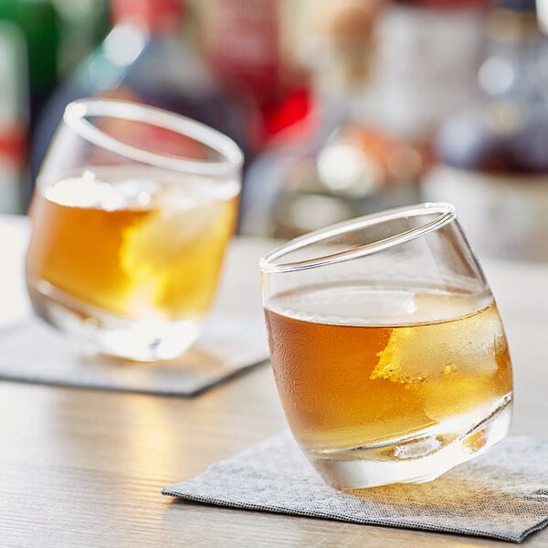 Two Acopa Select Old Fashioned glasses filled with brown liquid on a napkin.