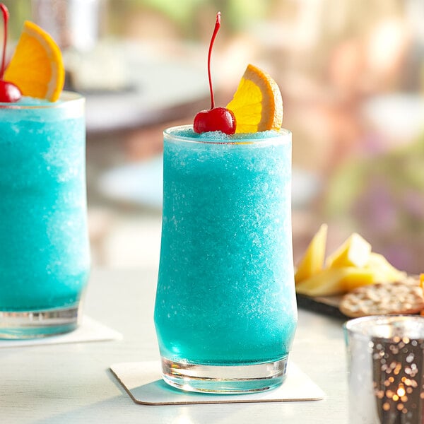 Two Acopa beverage glasses filled with blue cocktails garnished with orange slices and cherries.