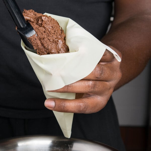 A person holding a Matfer Bourgeat nylon pastry bag filled with chocolate frosting.