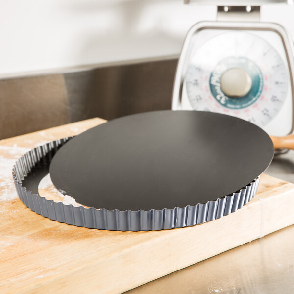 A black Matfer Bourgeat fluted quiche pan on a wooden surface.