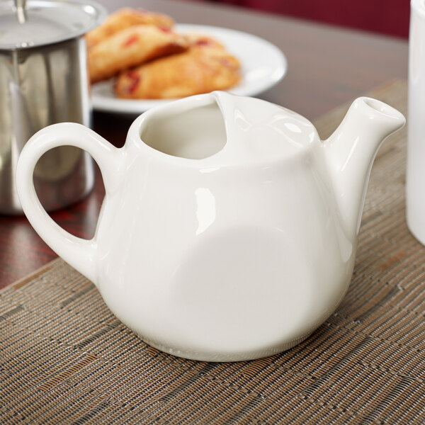 A white Tuxton China teapot on a table.
