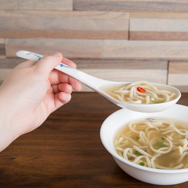 A person using a Thunder Group Blue Bamboo soup ladle over a bowl of soup.