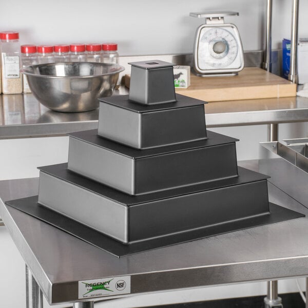 A stack of black square Matfer Bourgeat cake stands on a metal table.