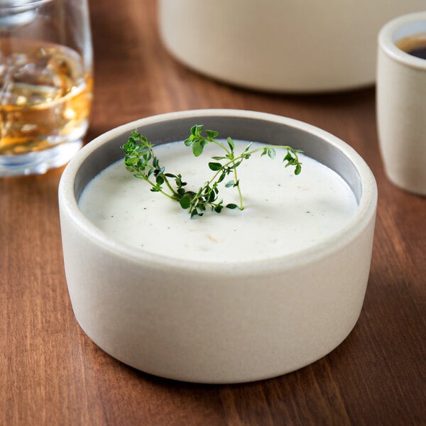 A Chef & Sommelier gray stoneware bowl filled with soup and garnished with a sprig of green leaves.
