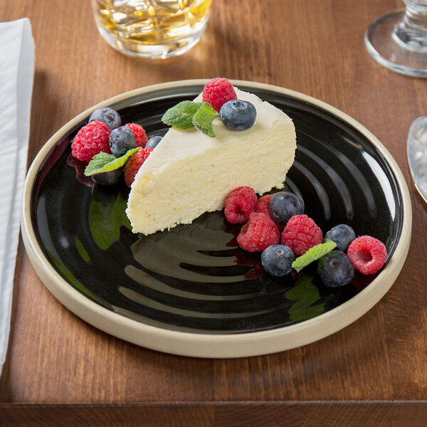 A slice of cheesecake with berries on a Chef & Sommelier black stoneware plate.