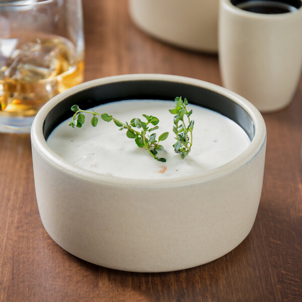 A black Chef & Sommelier stackable bowl with a sprig of herbs in it.